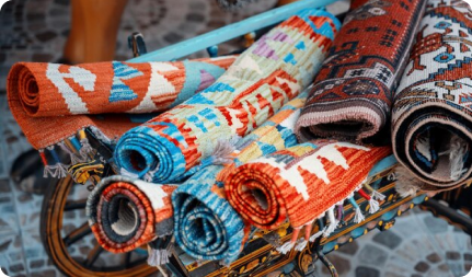 Colorful and vibrant carpet bag featuring a floral pattern in shades of blue, pink, and yellow, displayed against a plain background.